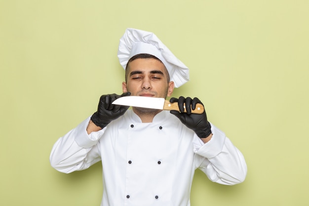 Free photo front view young male cook in white cook suit wearing dark gloves and holding knife on green