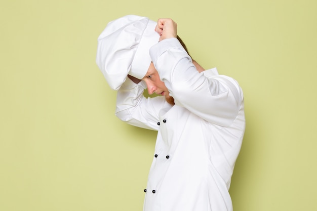 A front view young male cook in white cook suit wearing white head cap