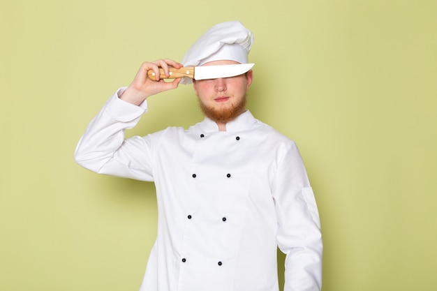칼로 그의 눈을 덮고 흰색 요리사 양복 흰색 머리 모자에 전면보기 젊은 남성 요리사