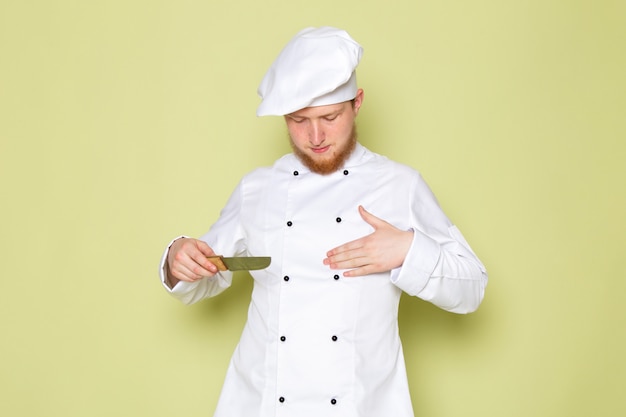 Вид спереди молодой мужчина повар в белом костюме повара белая шапка держит нож