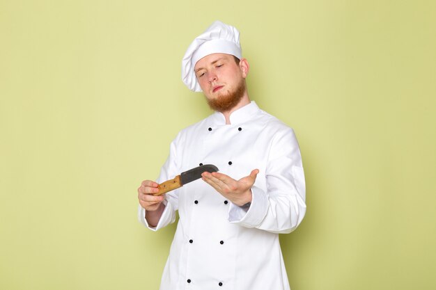 A front view young male cook in white cook suit white head cap holding knife