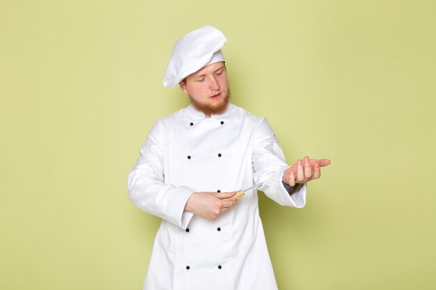 A front view young male cook in white cook suit white head cap holding knife