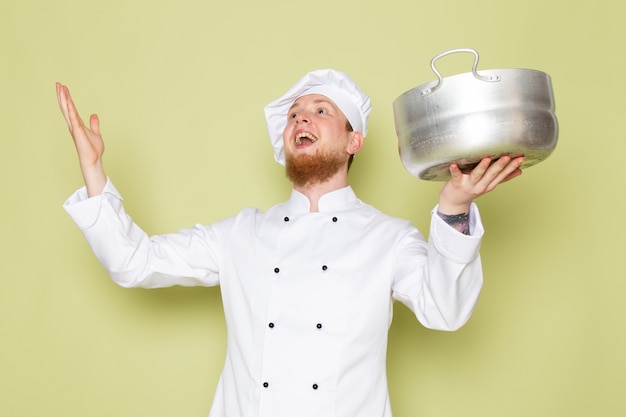 A front view young male cook in white cook suit white head cap holding silver saucepan amused excited