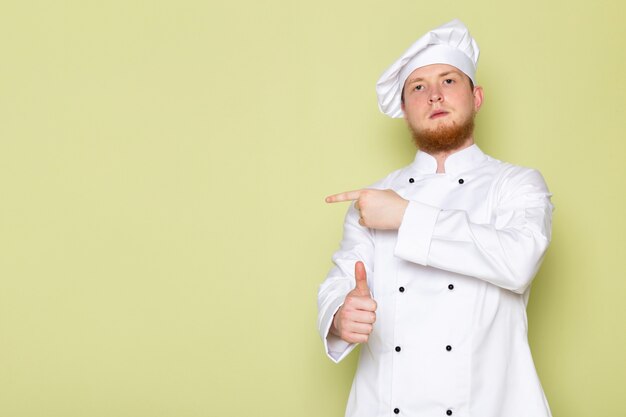 A front view young male cook in white cook suit white head cap pointing