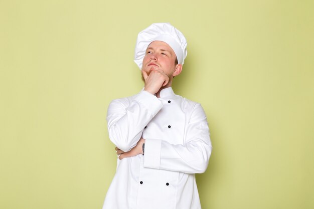 A front view young male cook in white cook suit white head cap posing thinking