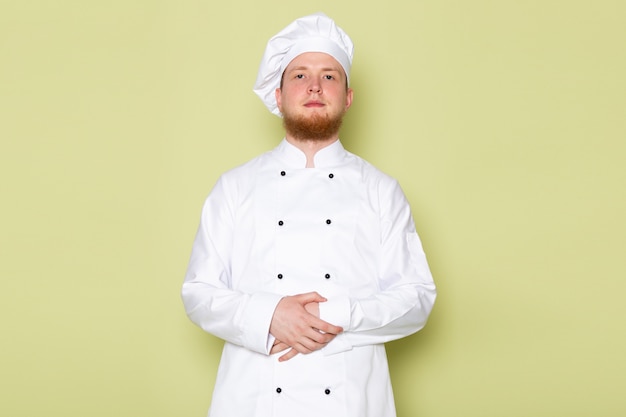 A front view young male cook in white cook suit white head cap standing