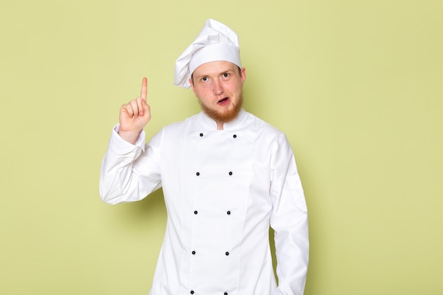 Вид спереди молодой самец повар в белом костюме повара белая шапка с поднятым пальцем
