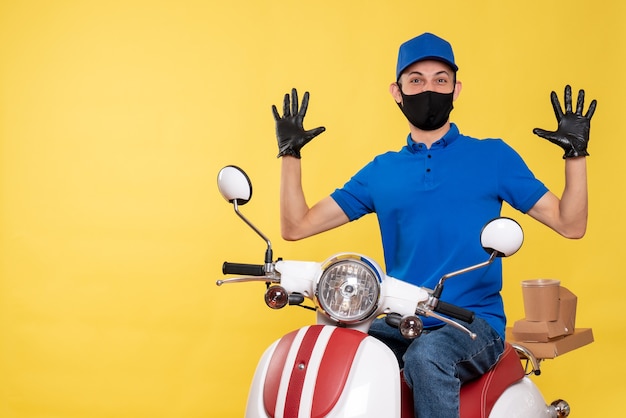 Front view young male courier in blue uniform and mask on a yellow background