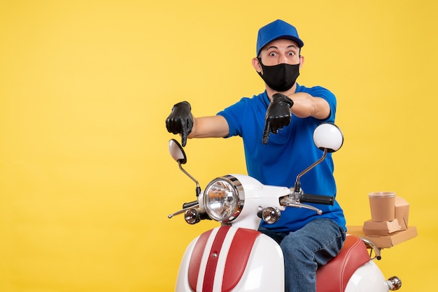 Front view young male courier in blue uniform on yellow background bike covid- pandemic service virus work delivery job