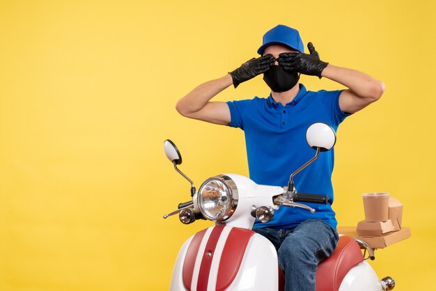 Front view young male courier in blue uniform on yellow background covid- pandemic service job virus bike delivery