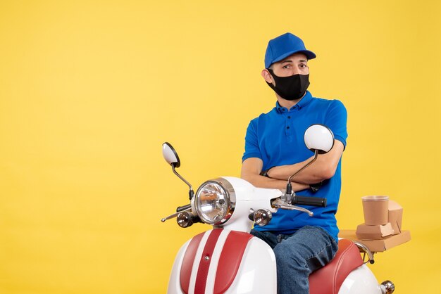 Front view young male courier in blue uniform on yellow background covid- pandemic service job virus work delivery