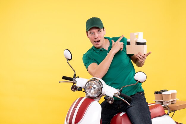 Front view young male courier in green uniform with coffee on yellow 