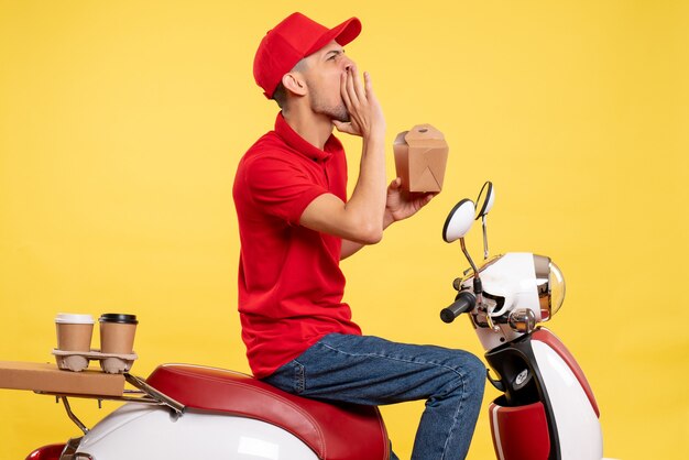 Front view young male courier in red uniform calling someone loudly on yellow background