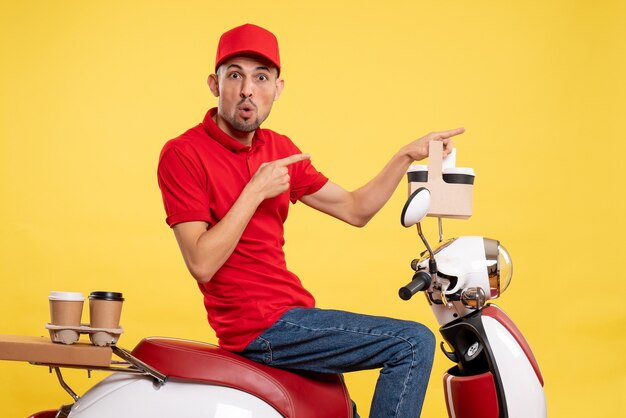 Front view young male courier in red uniform with coffee on yellow background