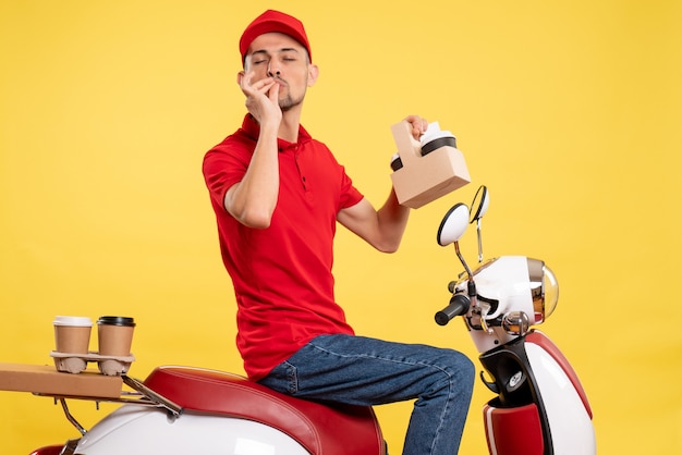 Front view young male courier in red uniform with coffee on yellow background