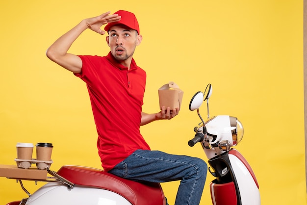 Front view young male courier in red uniform with delivery food on yellow background