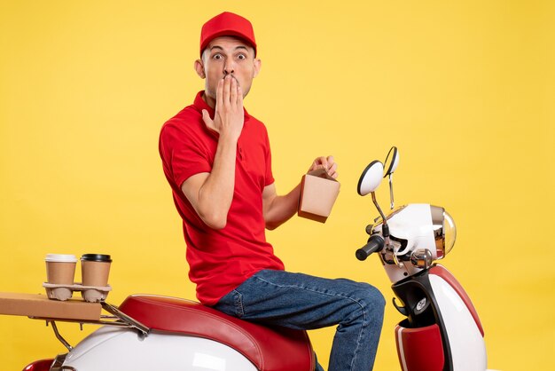 Front view young male courier in red uniform with delivery food on yellow background