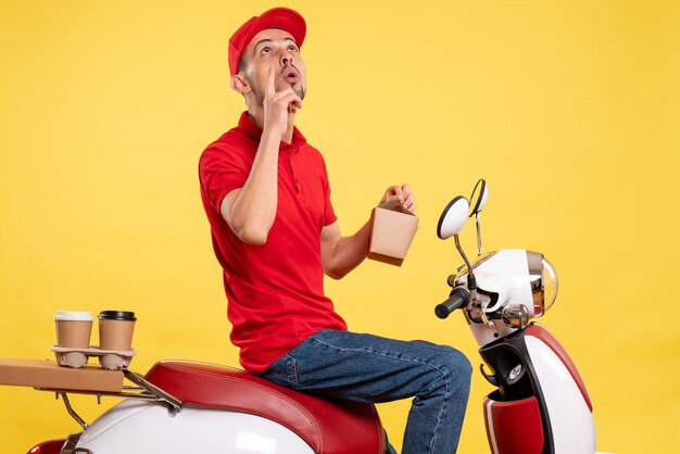 Front view young male courier in red uniform with delivery food on yellow background