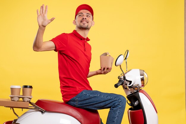 Front view young male courier in red uniform with delivery food on yellow background