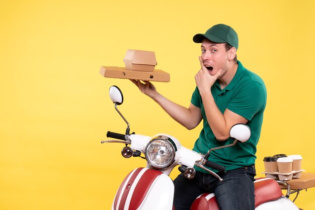 Front view young male courier in uniform holding food packages on the yellow 