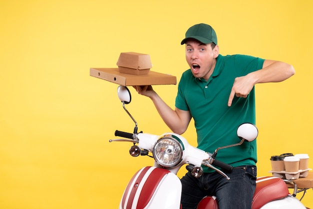 Front view young male courier in uniform holding food packages on yellow 