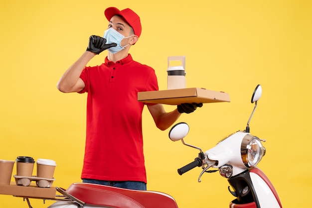 Front view young male courier in uniform with coffee and food box on a yellow background