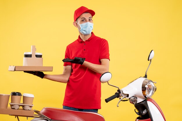 Front view young male courier in uniform with coffee and food box on yellow background