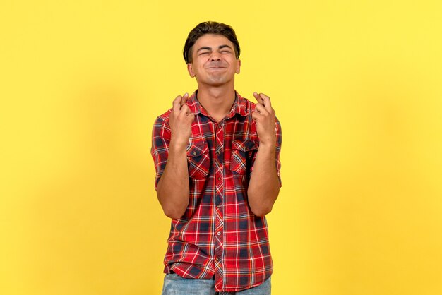 Front view young male crossing his fingers on yellow background male model color