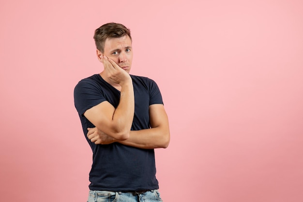 Front view young male in dark-blue shirt posing and feeling depressed on pink background