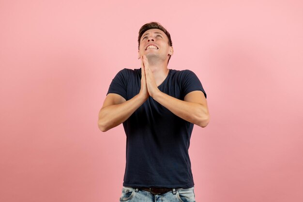 Front view young male in dark-blue shirt posing and praying on pink background