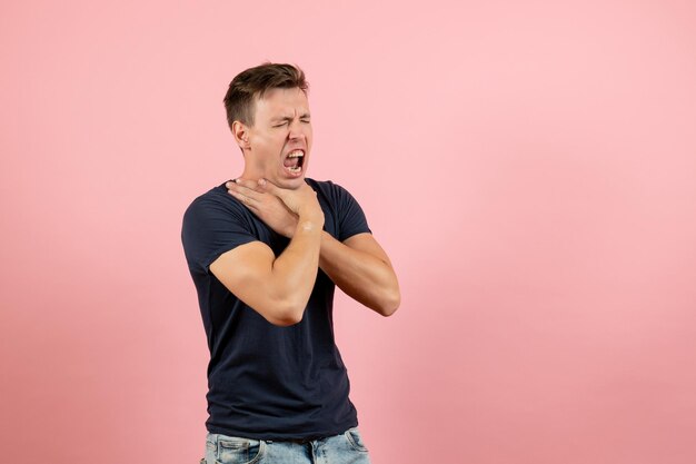 Front view young male in dark-blue t-shirt posing and choking himself on pink background