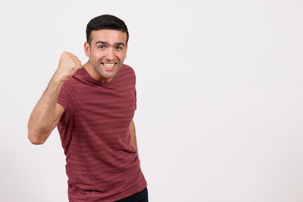 Front view young male in dark-red t-shirt posing and rejoicing on white background