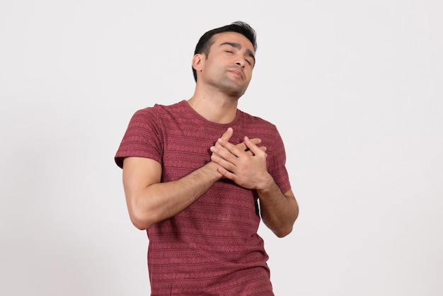 Front view young male in dark-red t-shirt touching his heart on white background