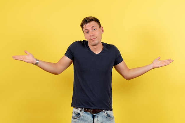 Front view young male in dark t-shirt and jeans posing on a yellow background