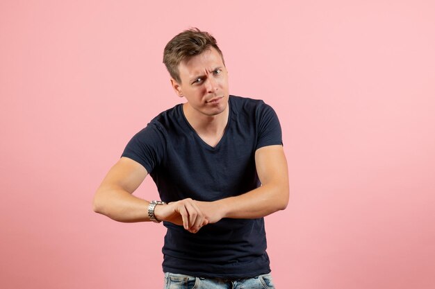 Front view young male in dark t-shirt looking at his wrist and checking time on a pink background