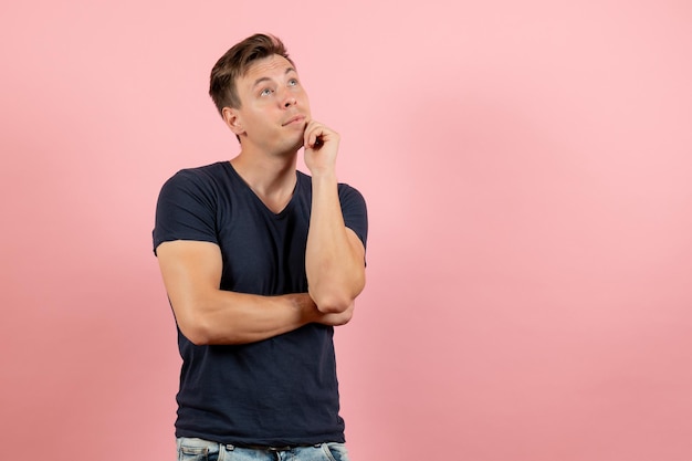 Front view young male in dark t-shirt posing and thinking on pink background