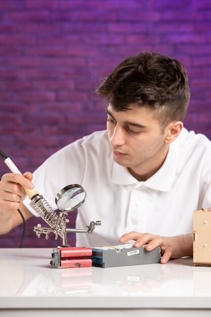 Front view young male behind desk trying to fix little construction on purple wall