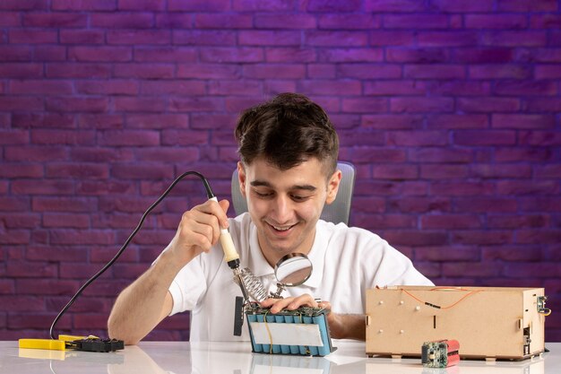 Front view young male behind desk trying to fix little house layout on purple wall