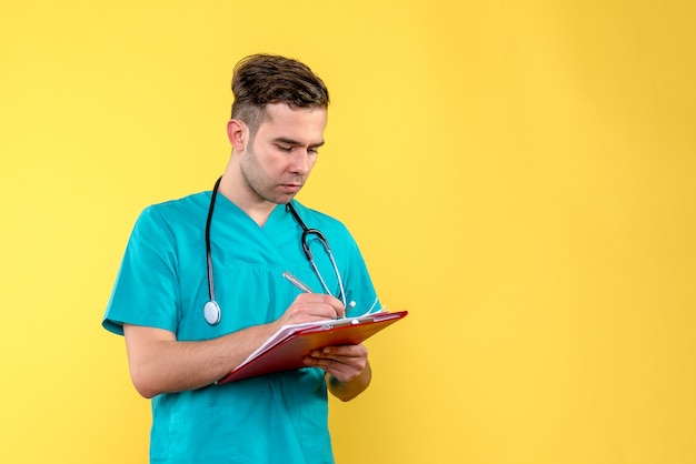 Free photo front view of young male doctor holding analyzes on a yellow wall