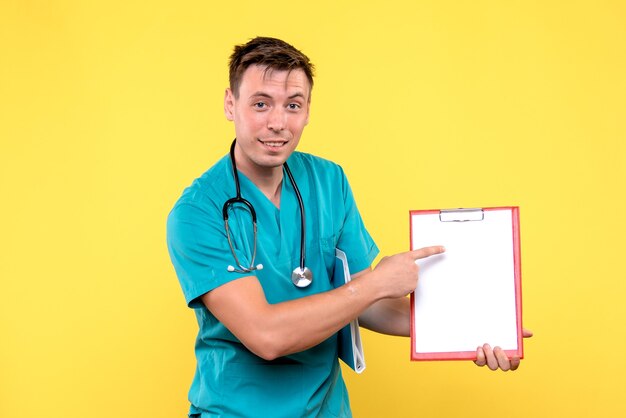 Front view of of young male doctor holding analyzes on yellow wall