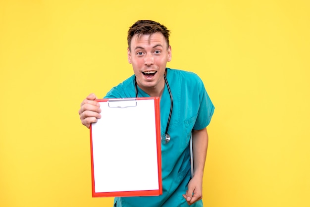 Front view of young male doctor holding analyzes on yellow wall