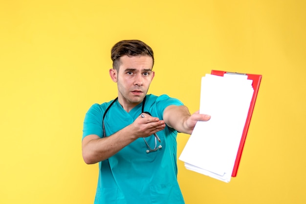 Вид спереди молодого мужчины-врача, держащего документы на желтой стене