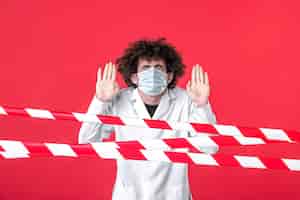 Бесплатное фото Вид спереди молодой врач-мужчина в медицинской форме и маске на красном фоне изолированная больница наркотики covid-предупреждение об опасности карантина