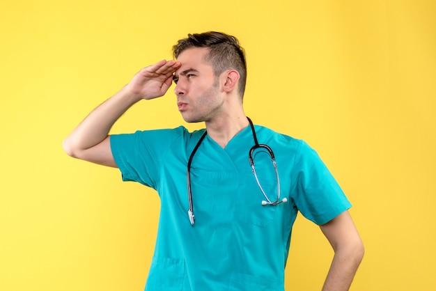 Foto gratuita vista frontale del giovane medico maschio guardando la distanza sulla parete gialla