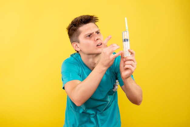 黄色の背景に注射を保持している医療スーツの若い男性医師の正面図