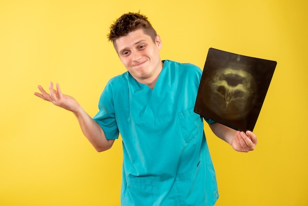 Вид спереди молодой мужчина-врач в медицинском костюме, держащий рентгеновский снимок на желтом фоне