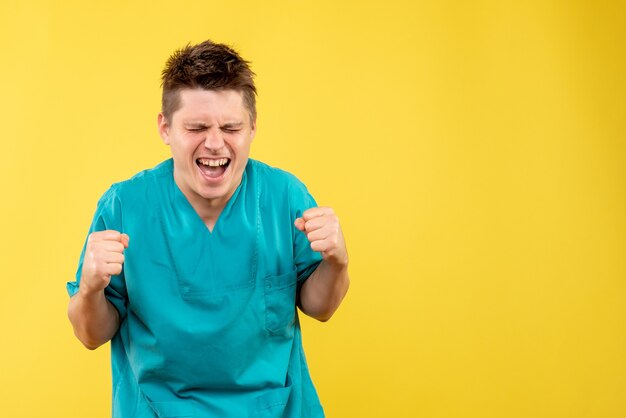 Front view young male doctor in medical suit rejoicing on a yellow background