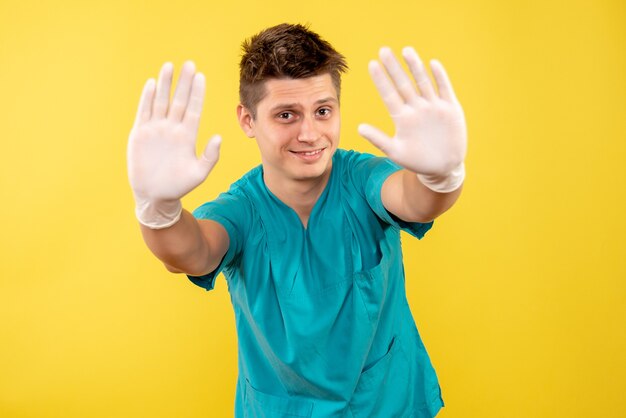 黄色の背景に手袋を着用した医療スーツの若い男性医師の正面図