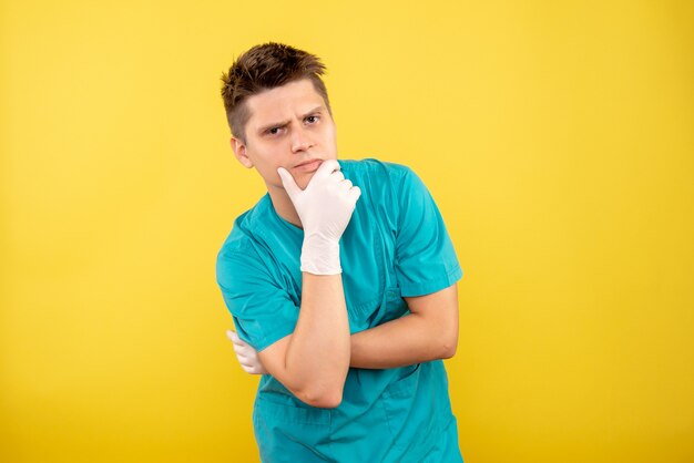 黄色の背景で考える手袋と医療スーツの若い男性医師の正面図