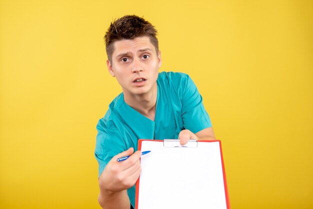 Front view young male doctor in medical suit with note and analysis on the yellow background